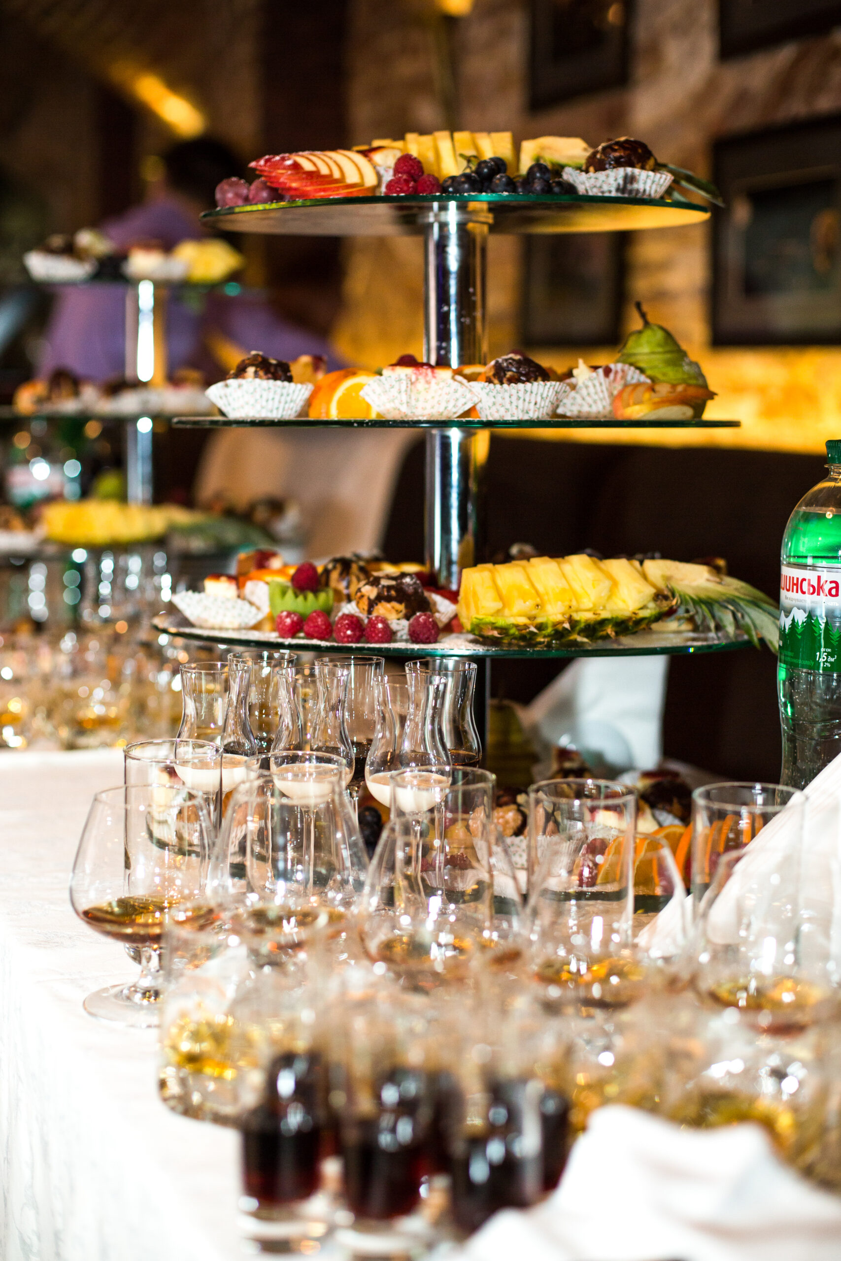 Glasses with alcohol stand before tired steel dish with sliced fruits